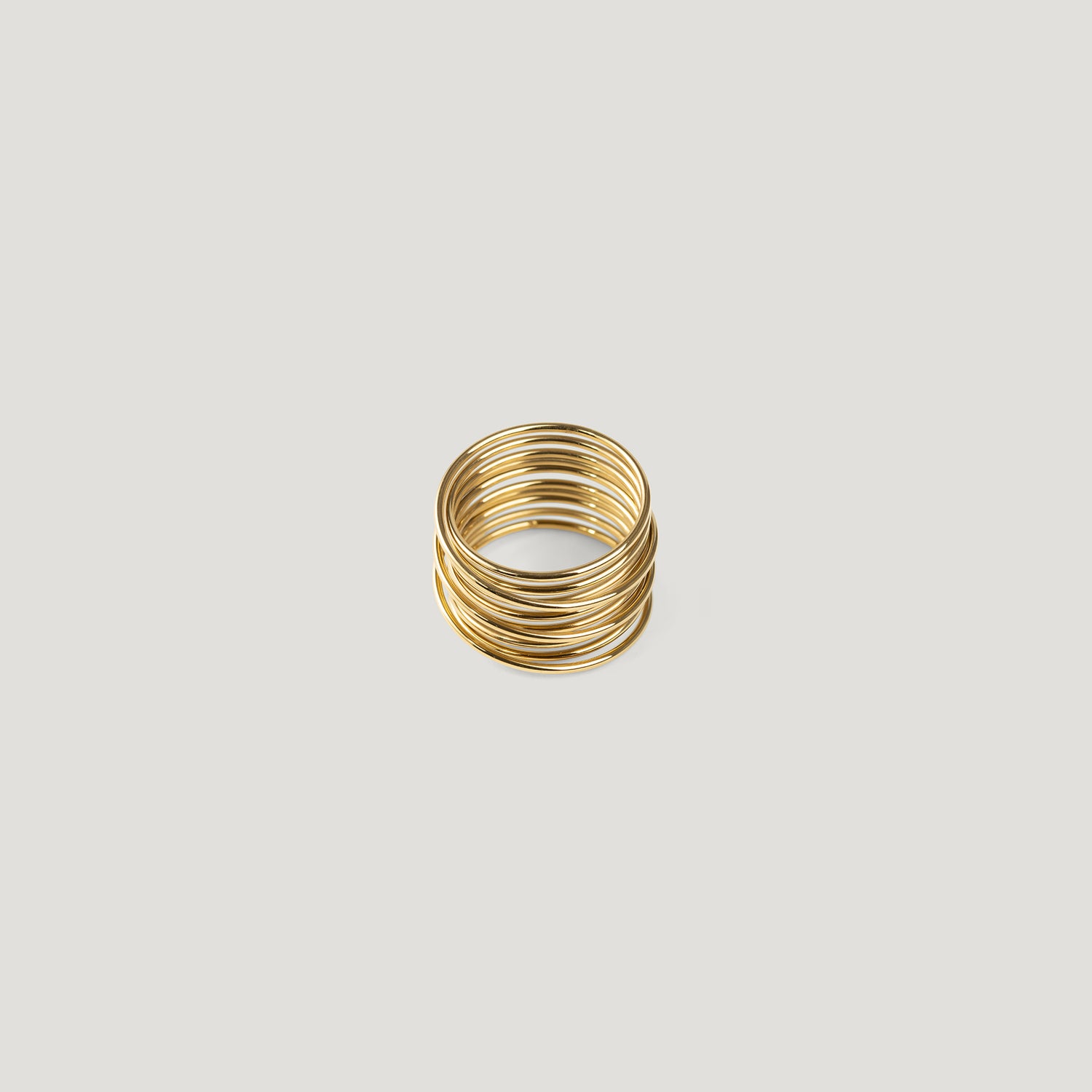 Gold statement ring made of tightly stacked wire coils, front view on light background.