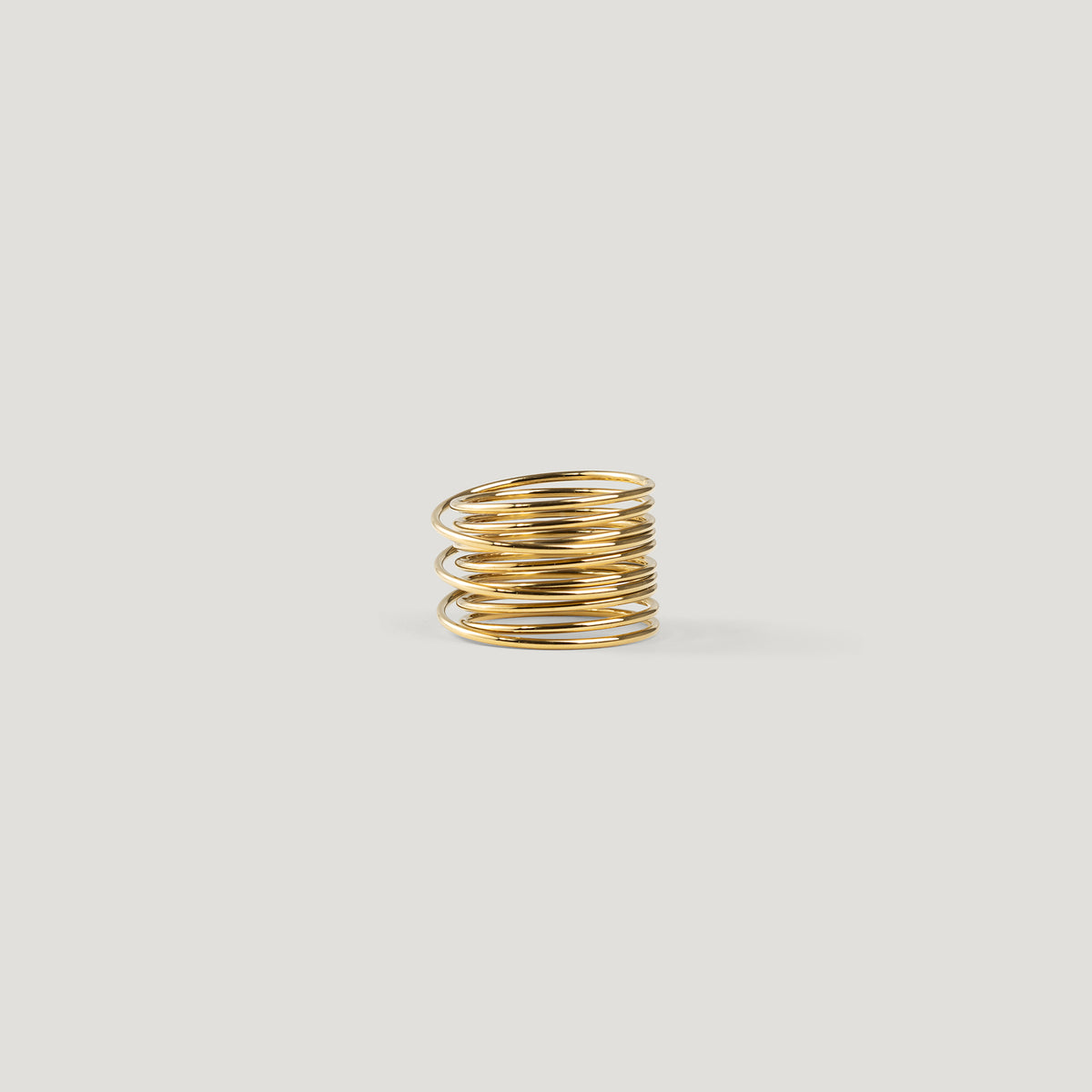 Gold statement ring made of tightly stacked wire coils, angled side view on light background.