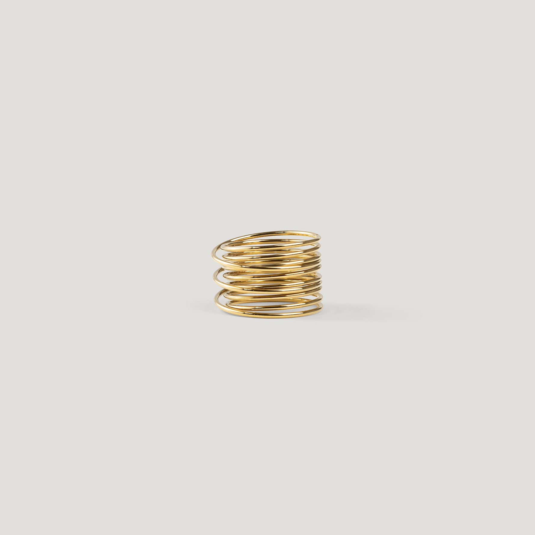 Gold statement ring made of tightly stacked wire coils, angled side view on light background.
