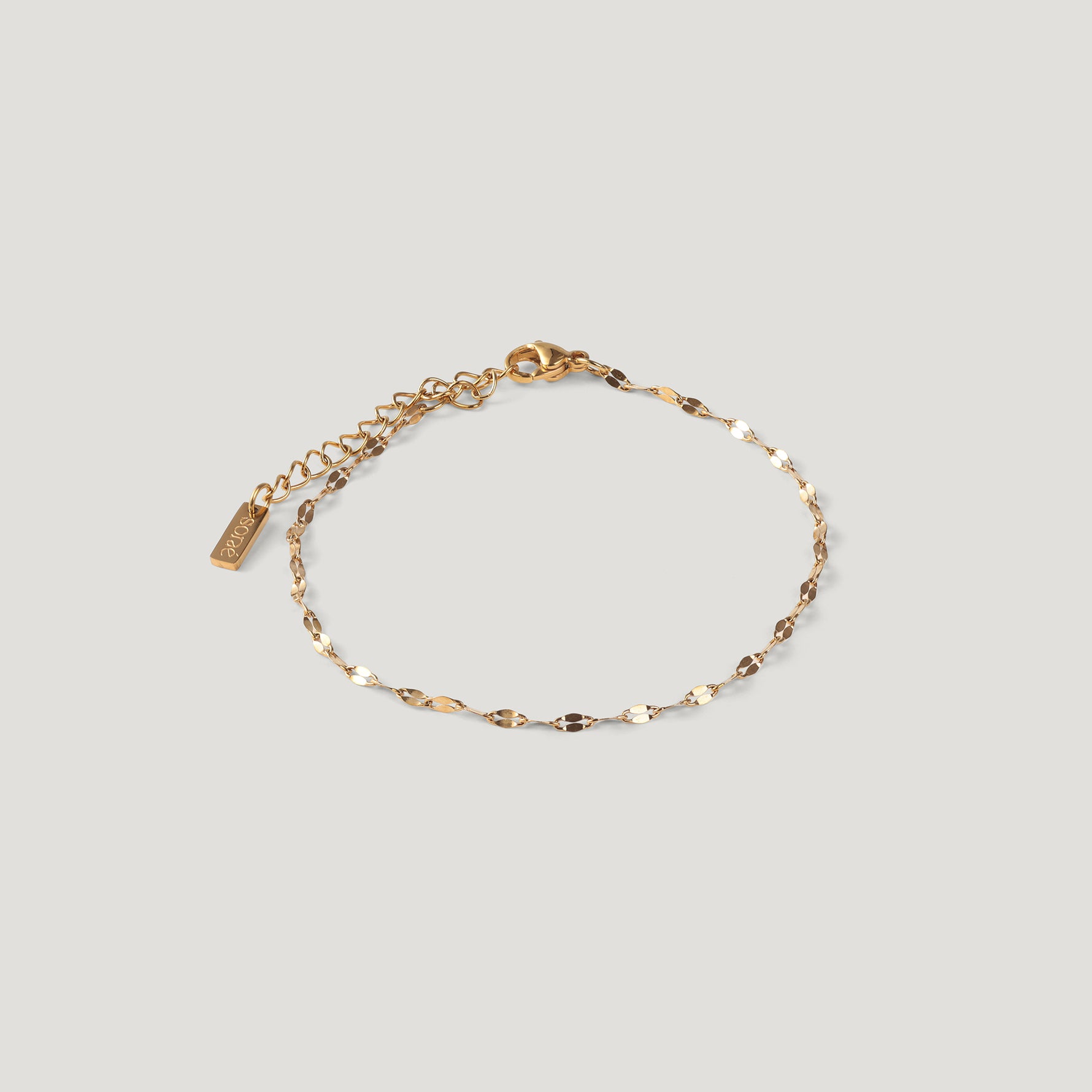 Delicate gold chain bracelet with flat oval links and a small tag charm, laid flat.