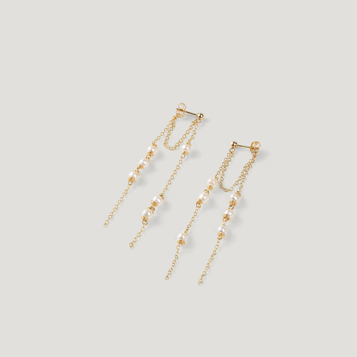 Pair of gold earrings with fringed pearl chains, fanned out on light background.