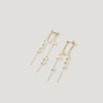 Pair of gold earrings with fringed pearl chains, fanned out on light background.