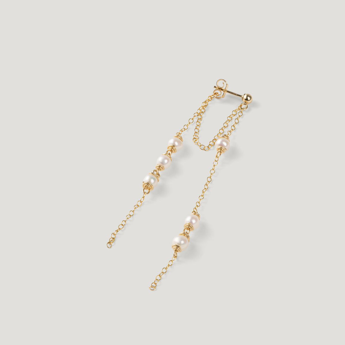 Single gold earring laid diagonally, showing two draping chains with pearls.