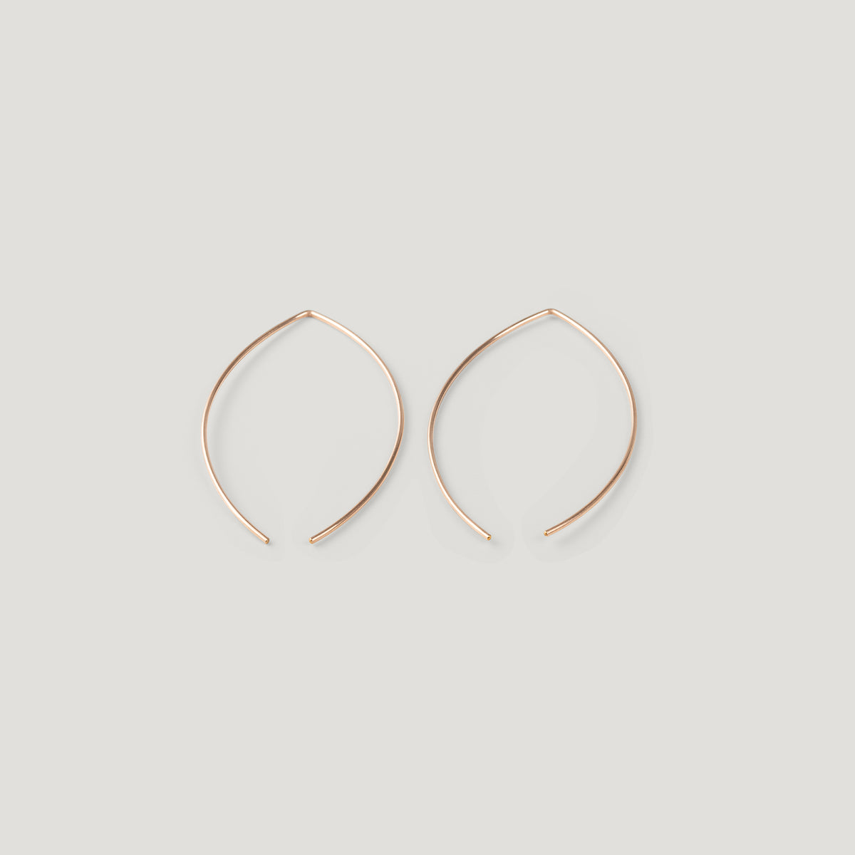 Pair of rose gold thread earrings in a pointed open-wire arc, laid flat.