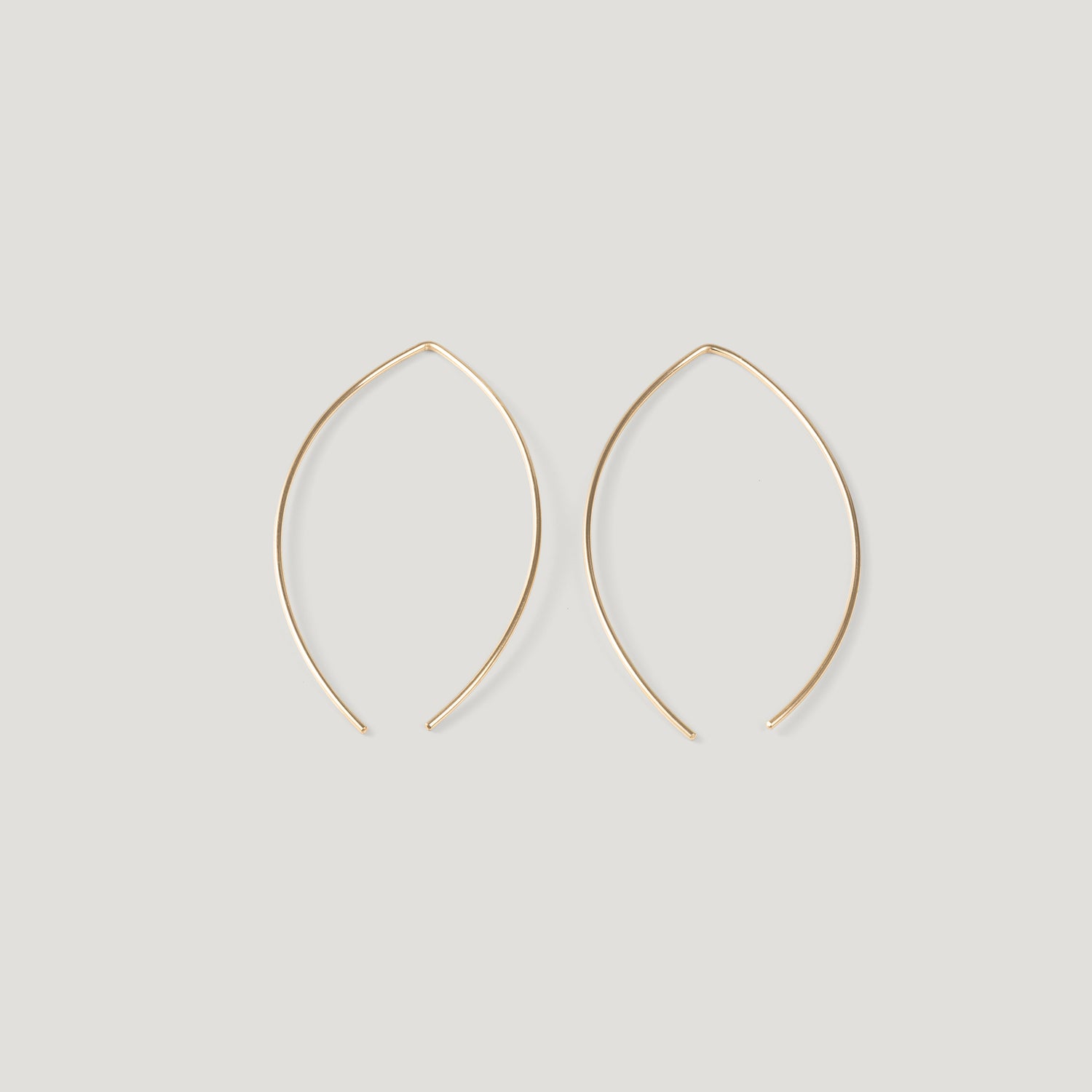 Pair of gold thread earrings in a pointed open-wire arc, laid flat.