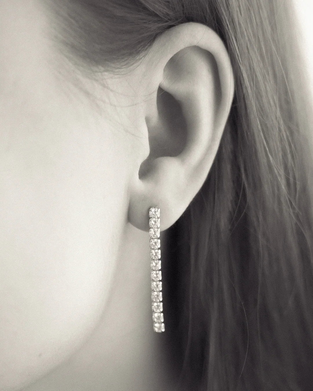 Close-up of a woman wearing a long, sparkling diamond drop earring