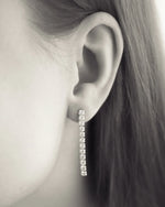 Close-up of a woman wearing a long, sparkling diamond drop earring