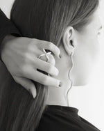 Woman wearing sculptural silver ring and wavy diamond drop earring