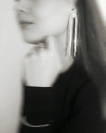Woman wearing long, sparkling rhinestone statement earrings with elegant, modern style.