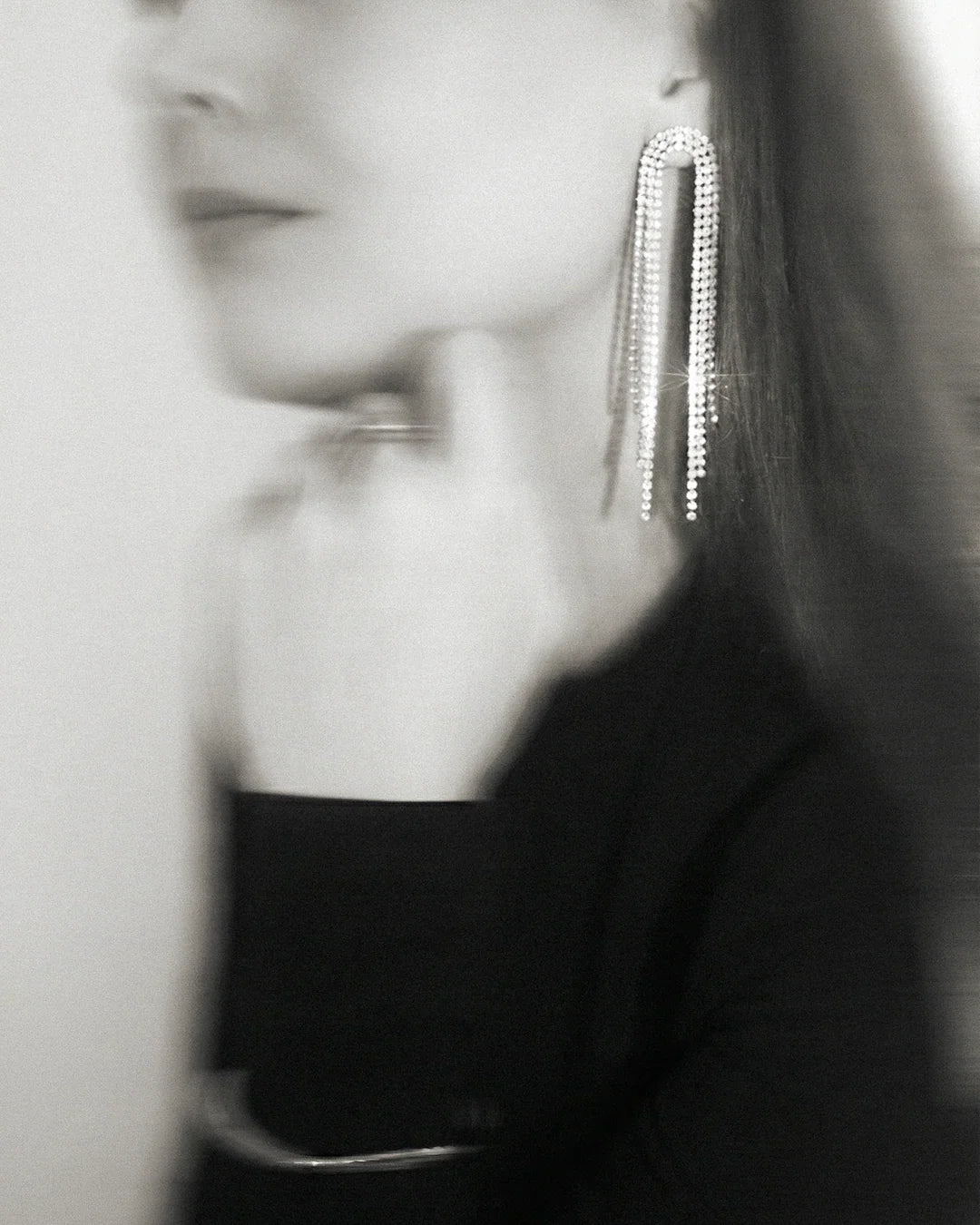 Woman wearing long, sparkling rhinestone statement earrings with elegant, modern style.