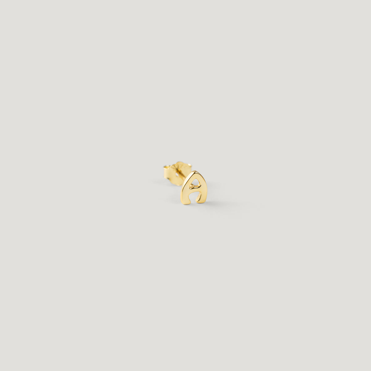 Single gold letter A initial stud earring, close-up on light background.