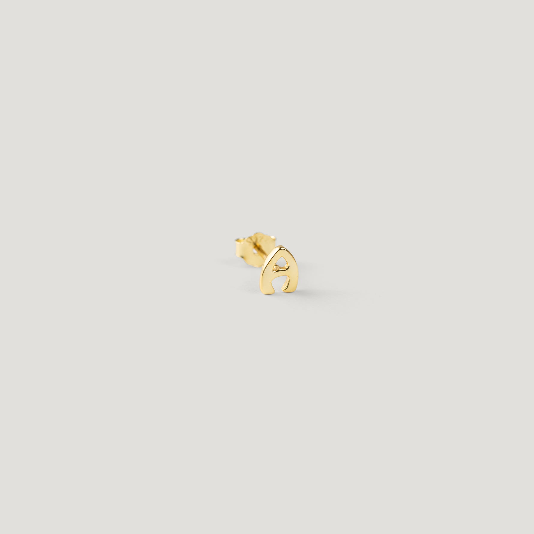 Single gold letter A initial stud earring, close-up on light background.