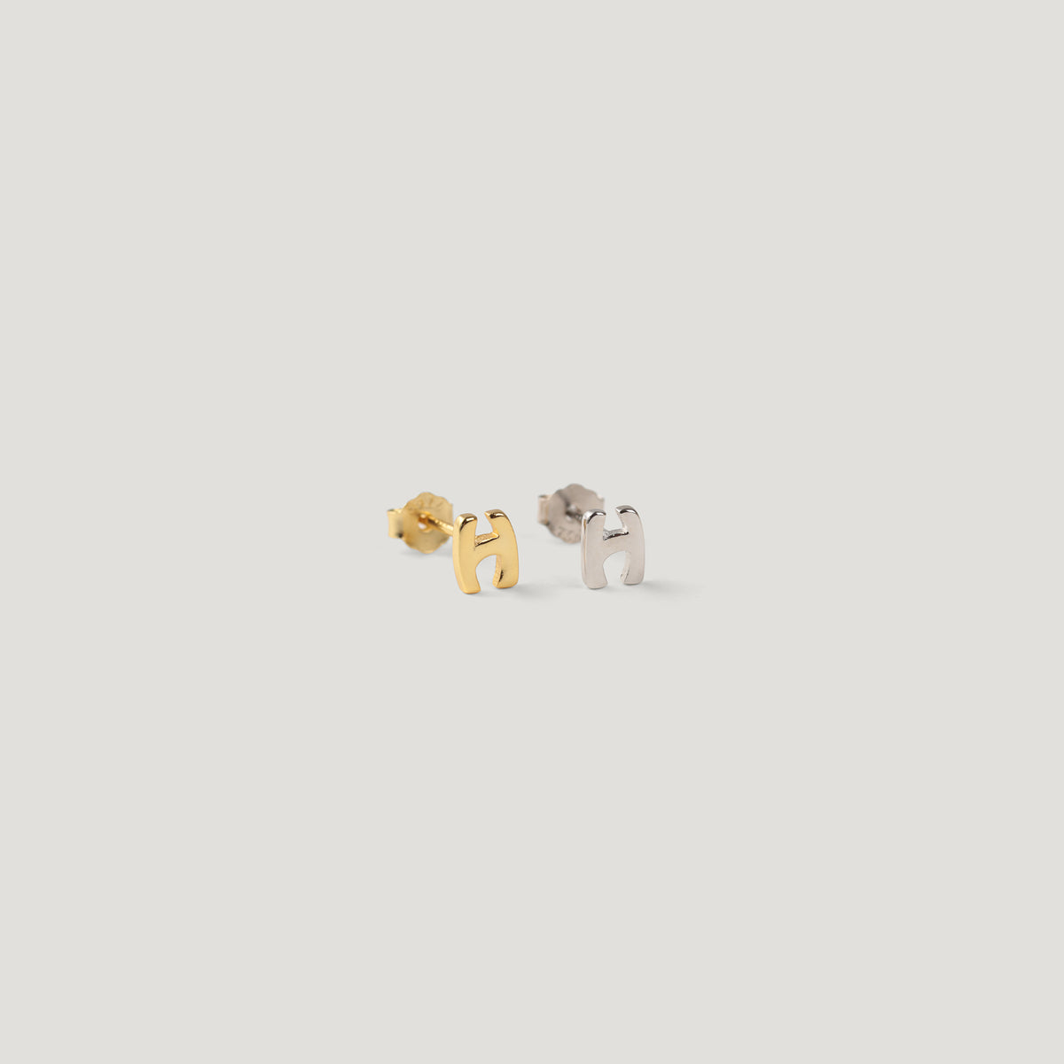 Gold and silver letter H initial stud earrings side by side on light background.