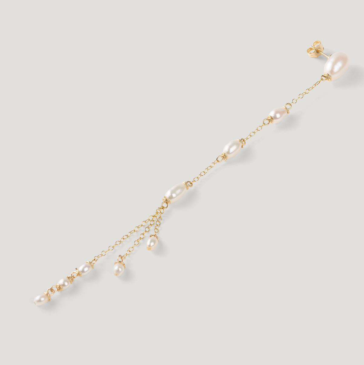 Single gold pearl drop earring laid diagonally, pearl tassel end, on light background.