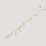 Single gold pearl drop earring laid diagonally, pearl tassel end, on light background.