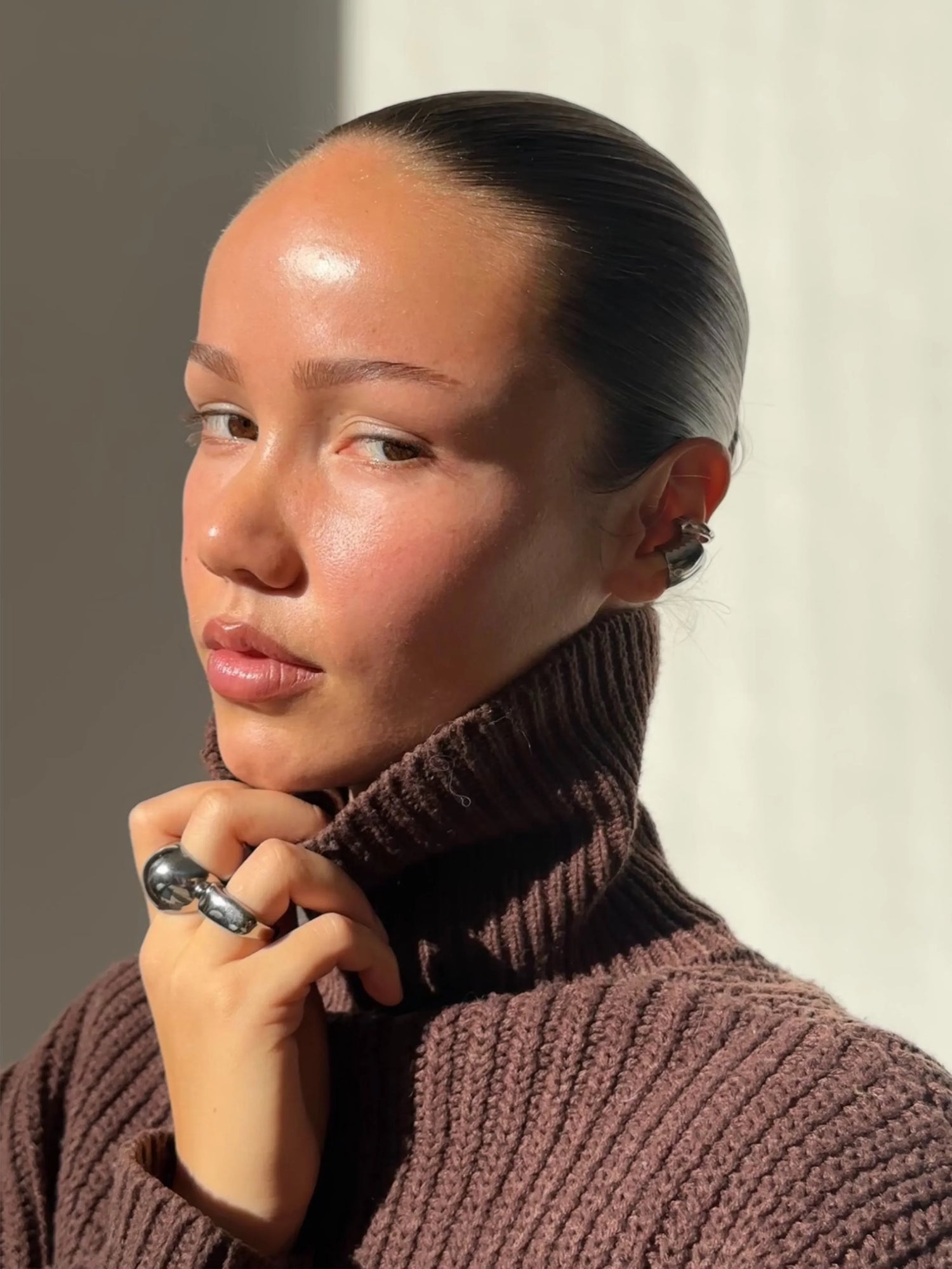 Woman wearing chunky silver ring and ear cuff, brown ribbed turtleneck, natural light