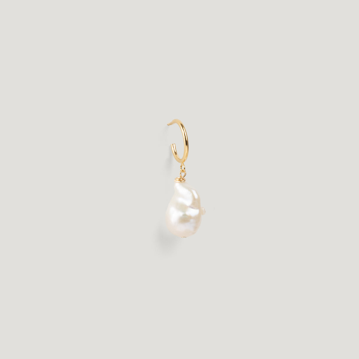 Close-up of a gold hoop earring with an irregular baroque pearl drop on light background.