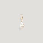 Close-up of a gold hoop earring with an irregular baroque pearl drop on light background.