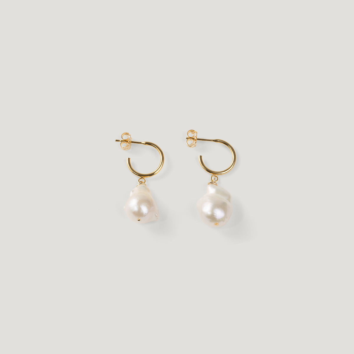Pair of gold hoop earrings with irregular baroque pearl drops on light background.
