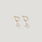 Pair of gold hoop earrings with irregular baroque pearl drops on light background.