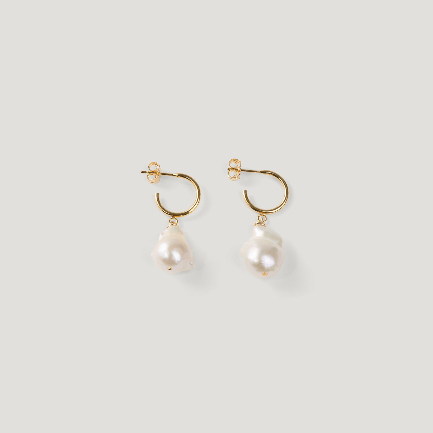 Pair of gold hoop earrings with irregular baroque pearl drops on light background.