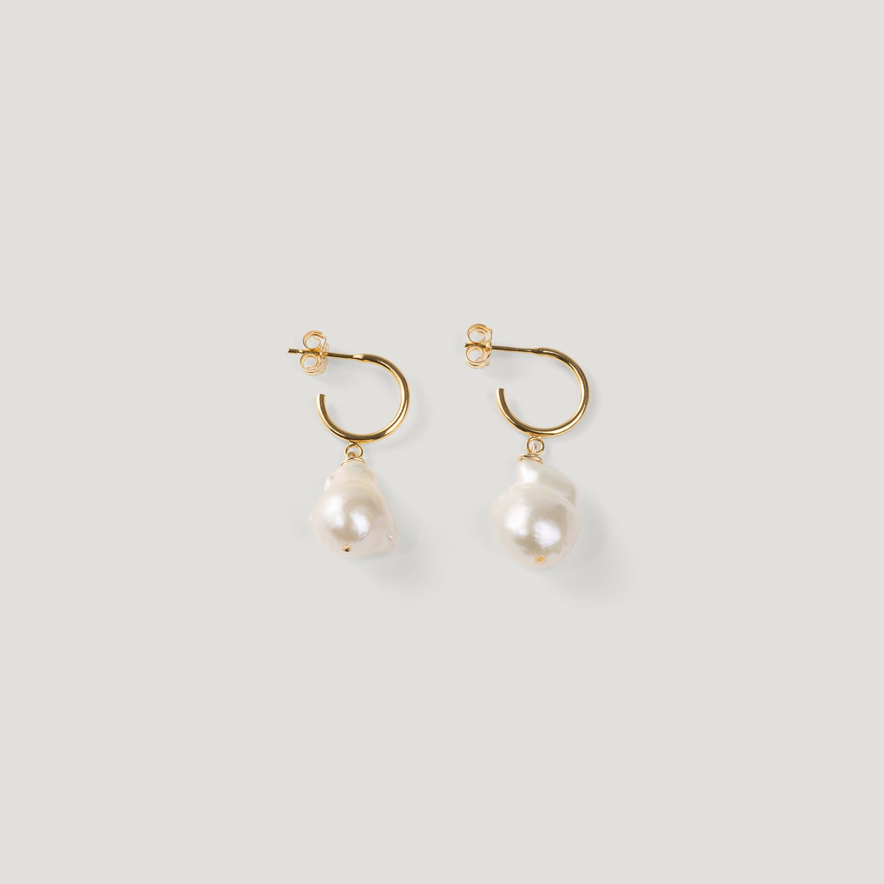 Pair of gold hoop earrings with irregular baroque pearl drops on light background.