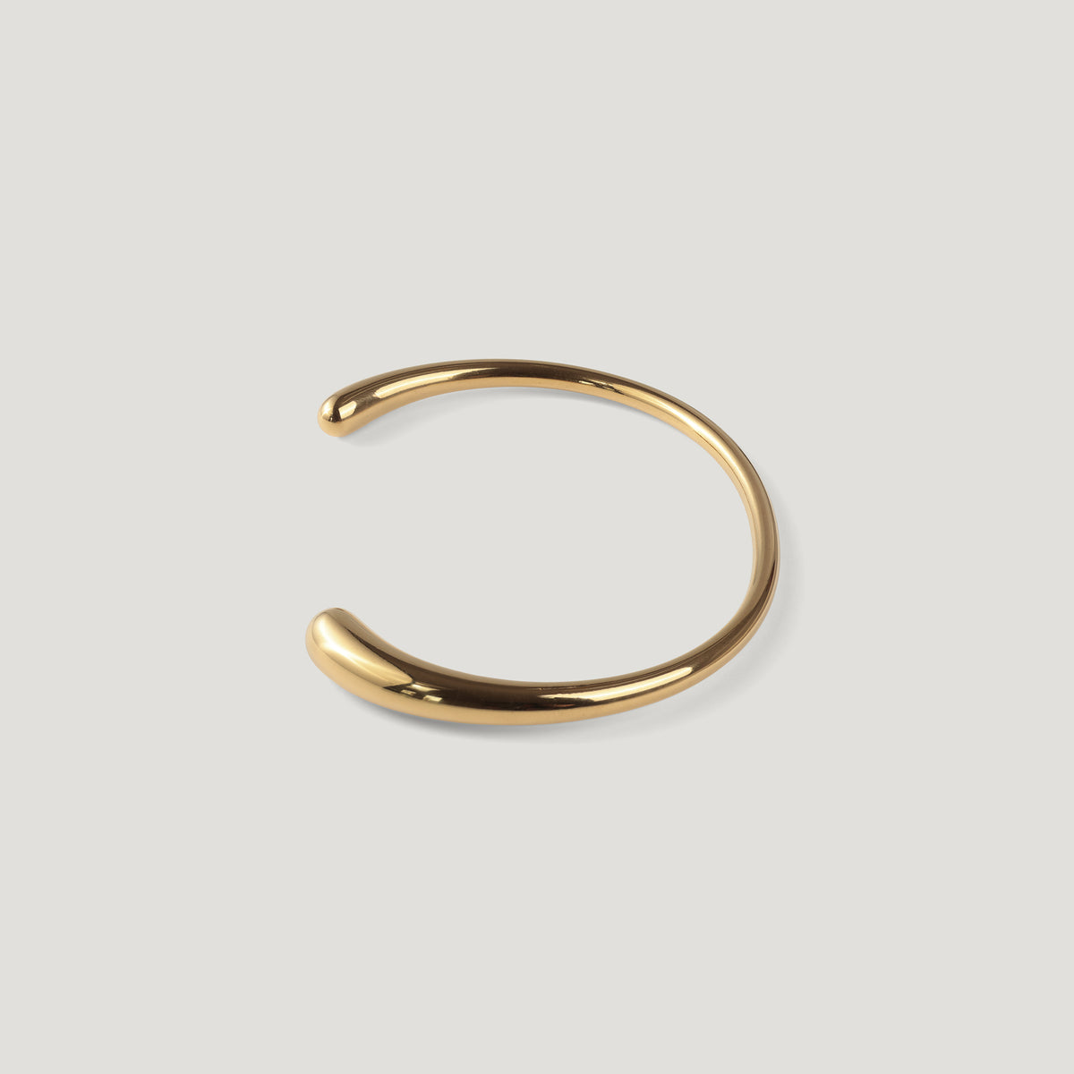 Gold open cuff bangle standing upright, showing its curved rounded shape, on light background.