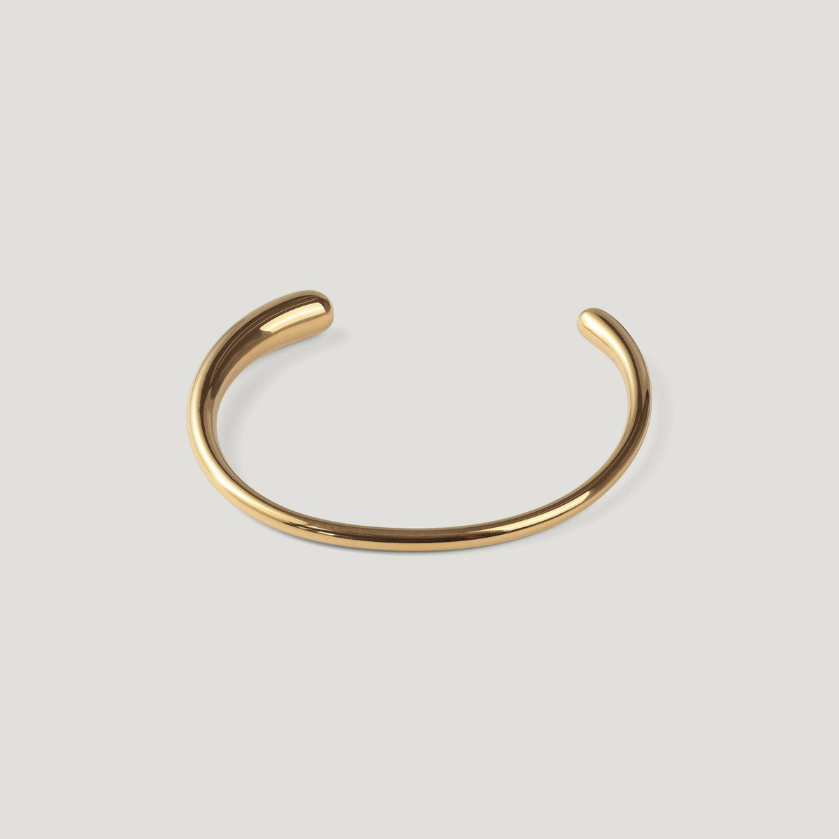 Gold open cuff bangle with a smooth rounded band, laid flat on light background.