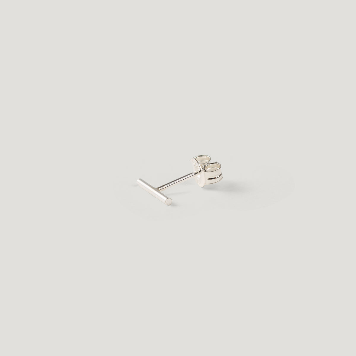 Single silver bar stud earring, showing post and back, on light background.