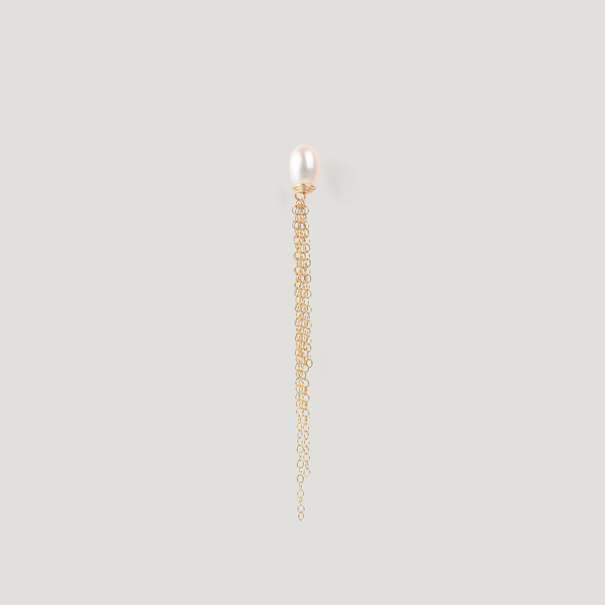Gold earring with a freshwater pearl stud and fine chain tassel on light background