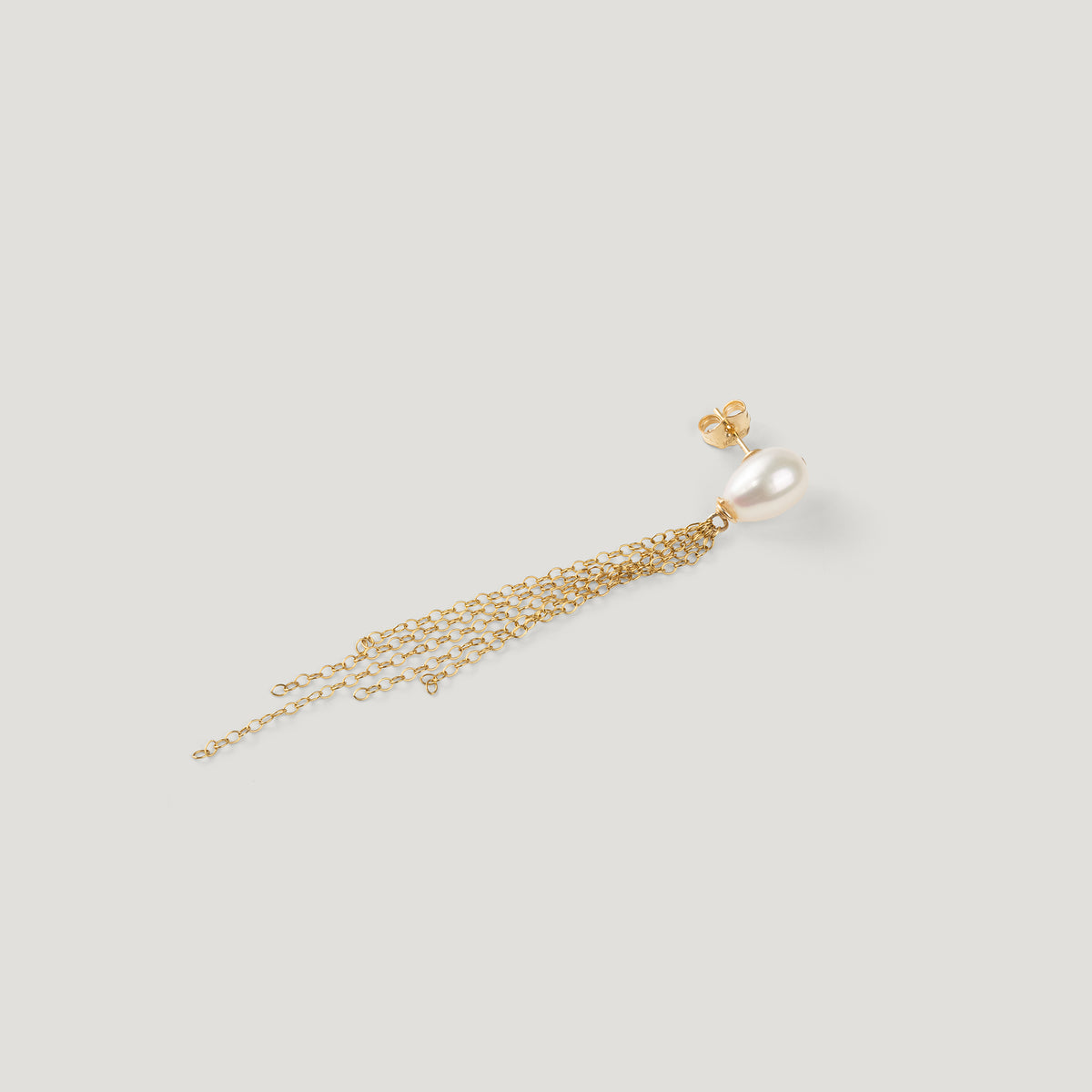 Gold earring lying flat, showing pearl stud, post fastening, and chain tassel on light background