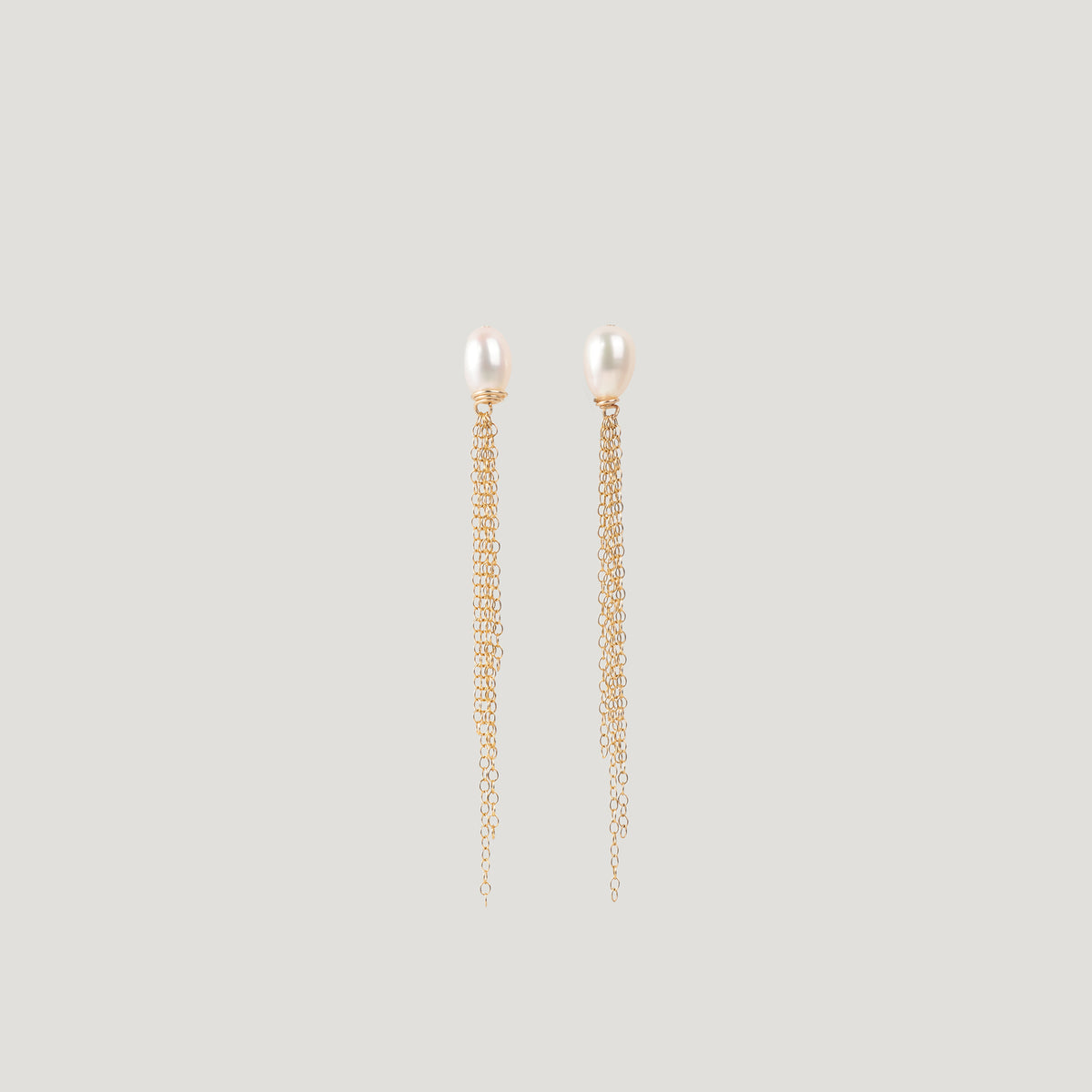 Pair of gold earrings with freshwater pearl studs and dangling chain tassels on light background