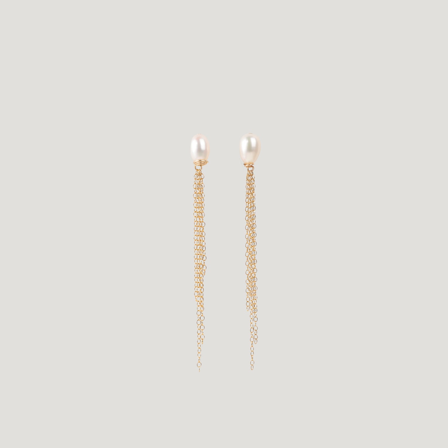 Pair of gold earrings with freshwater pearl studs and dangling chain tassels on light background