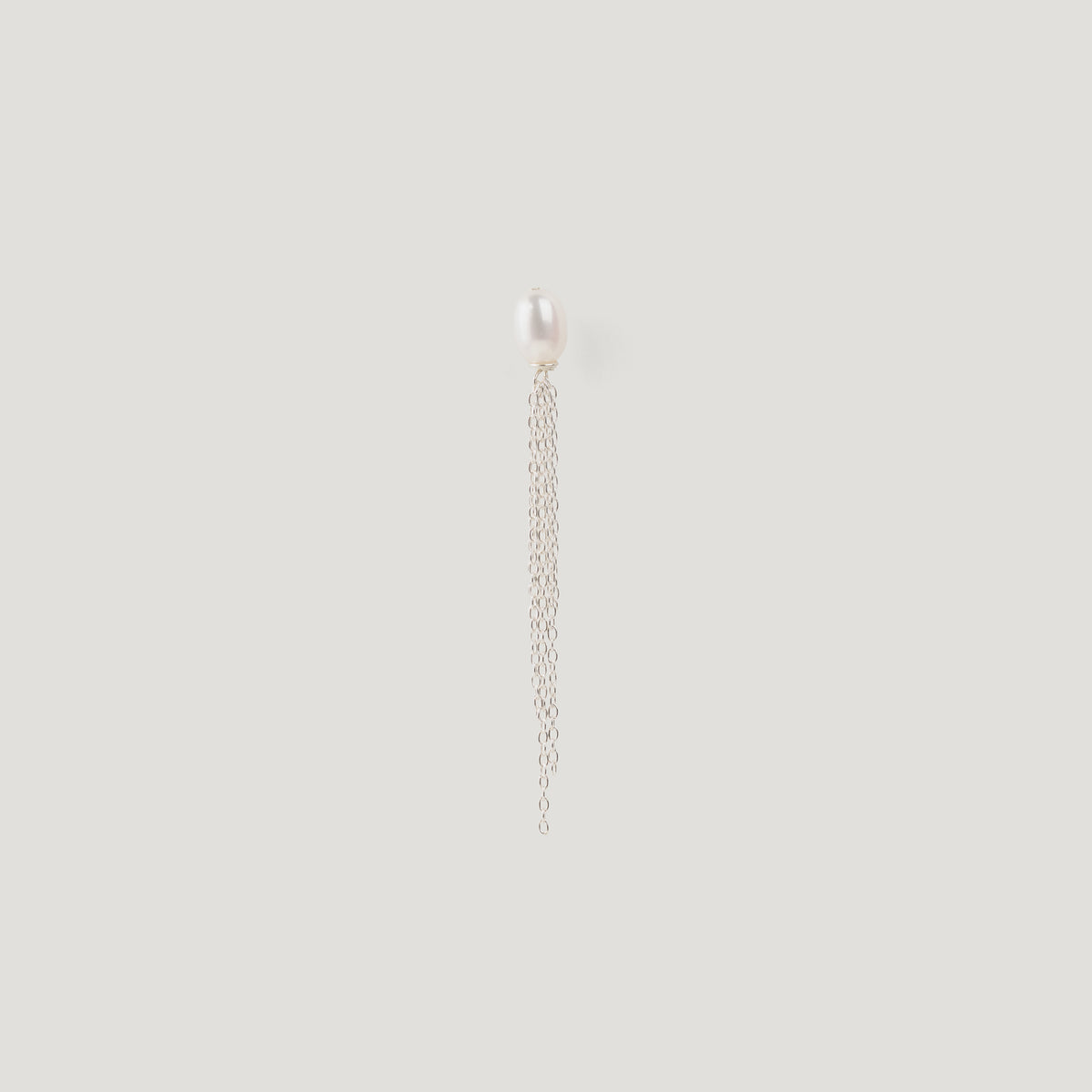 Silver earring with a freshwater pearl stud and dangling chain tassel on light background