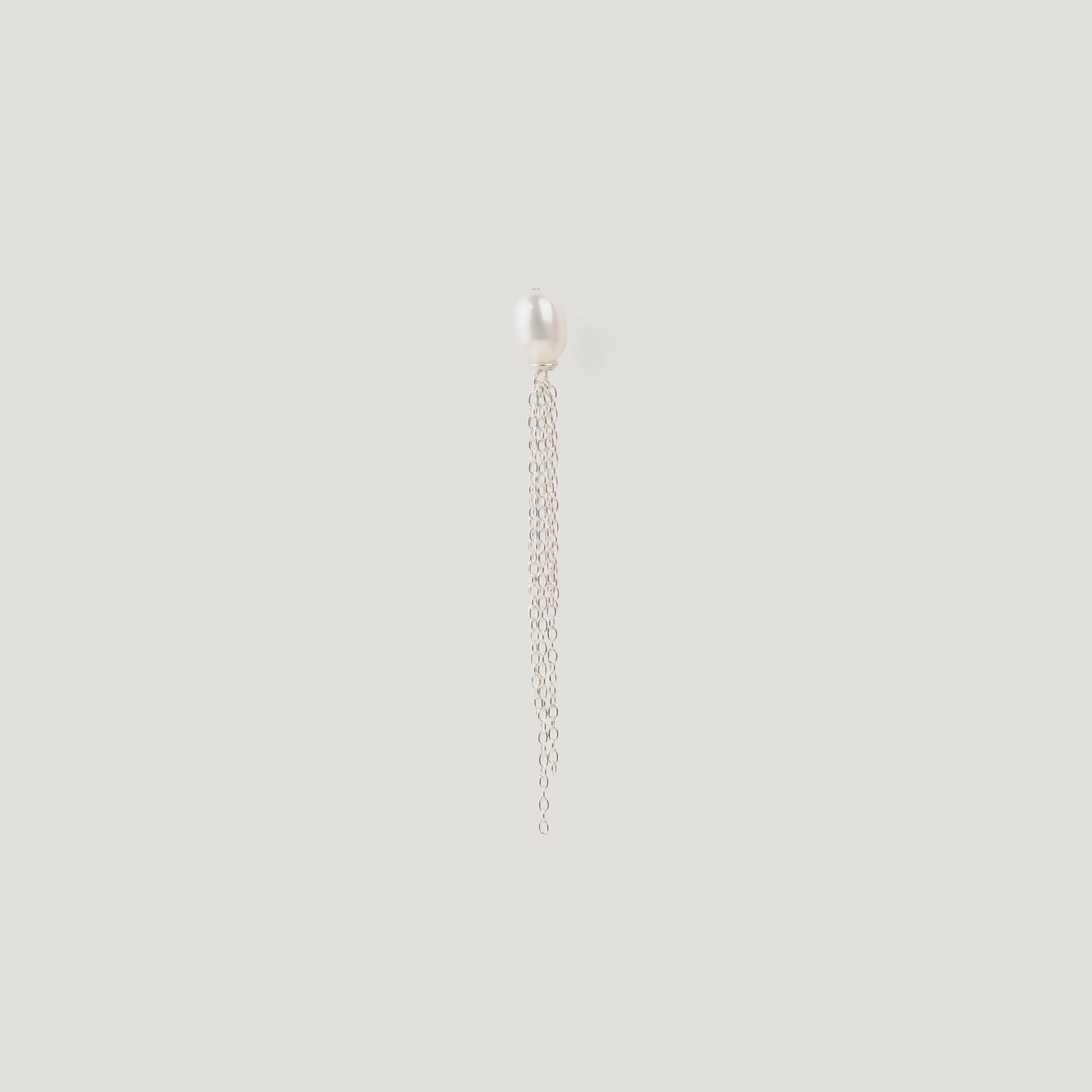 Silver earring with a freshwater pearl stud and dangling chain tassel on light background
