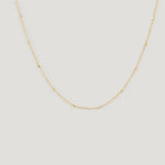 Gold satellite chain necklace with small bead stations, draped on light background.