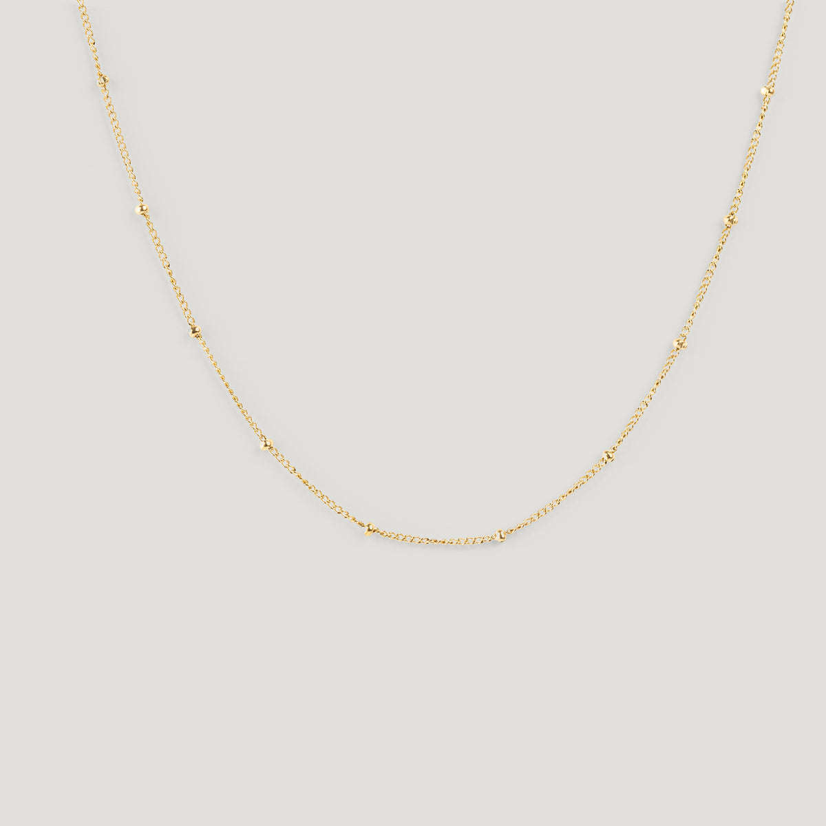 Gold satellite chain necklace with small bead stations, draped on light background.