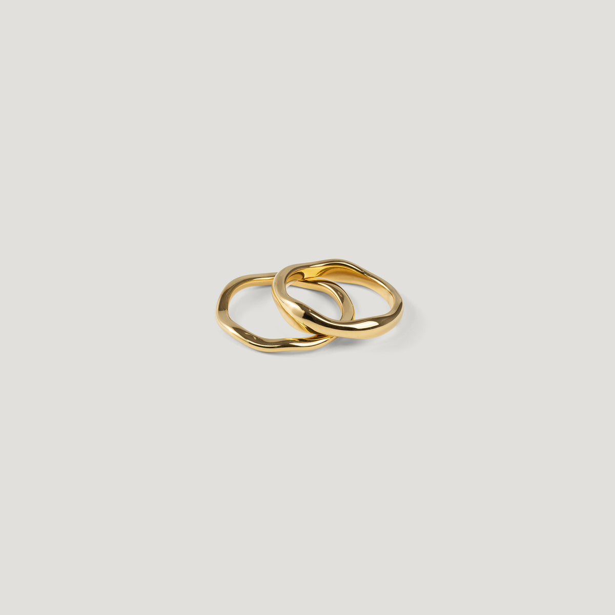 Two organic wavy gold rings interlocked and lying flat, one slim, one wider.