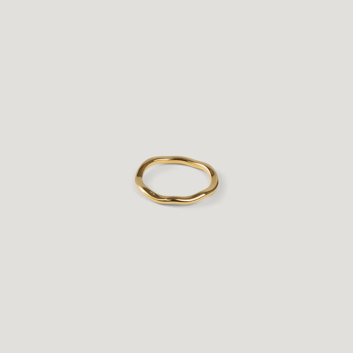 Small gold ring with an irregular wavy band, top-down view on light background.