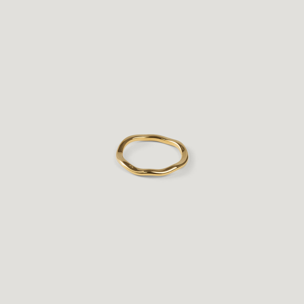 Small gold ring with an irregular wavy band, top-down view on light background.