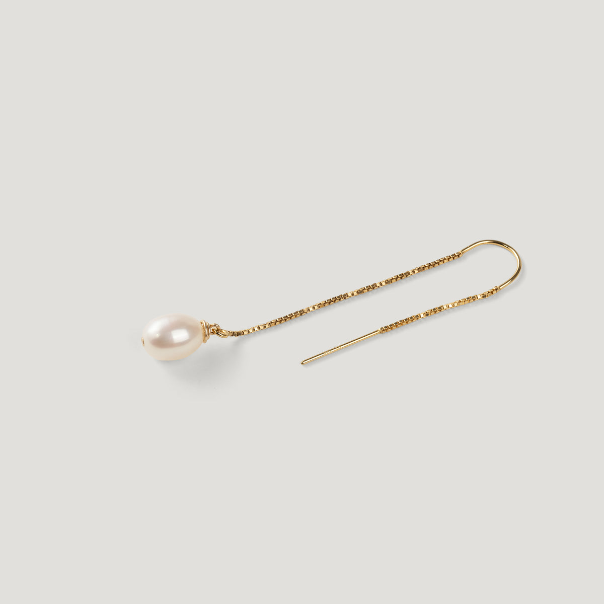 Gold thread earring with a pearl drop, chain laid diagonally on light background.