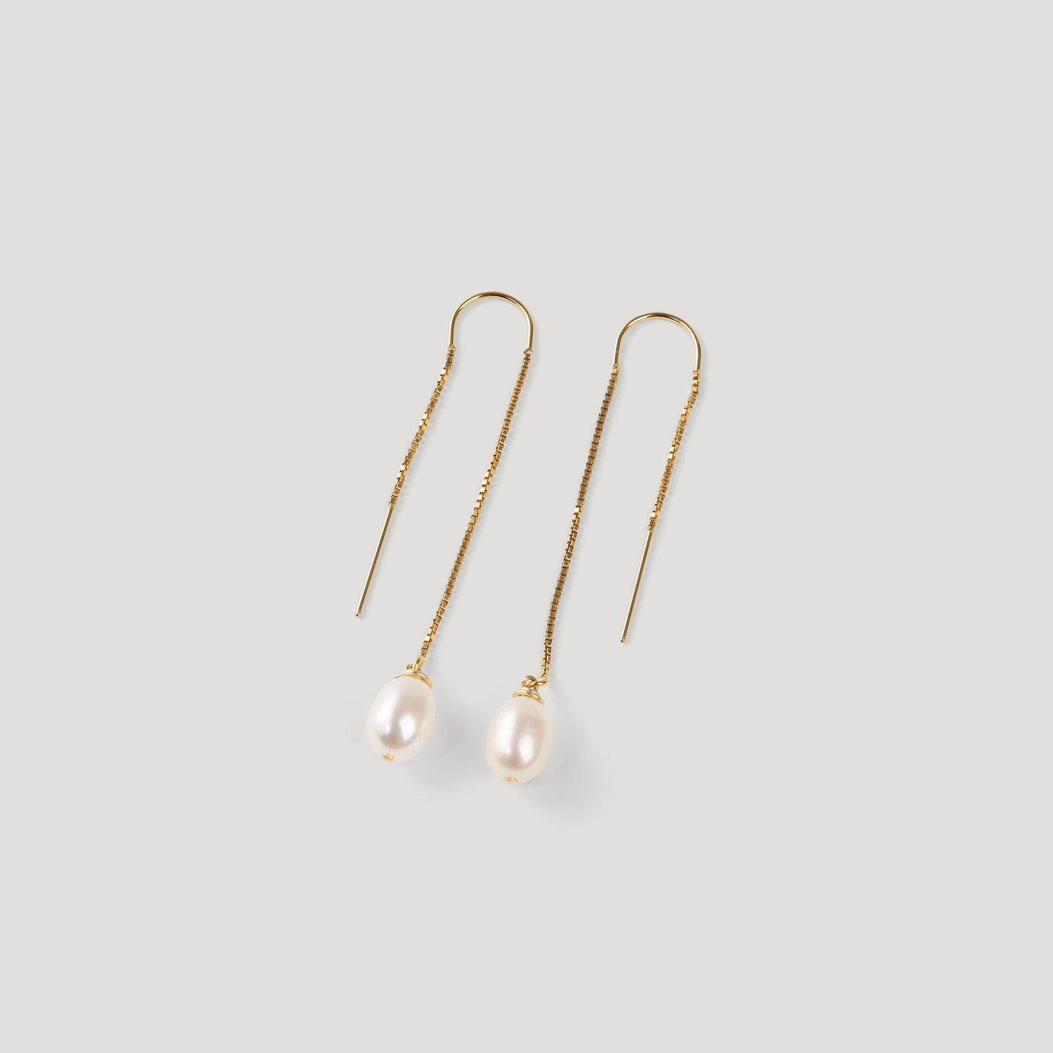Pair of gold thread earrings, each with a dangling pearl, on light background.