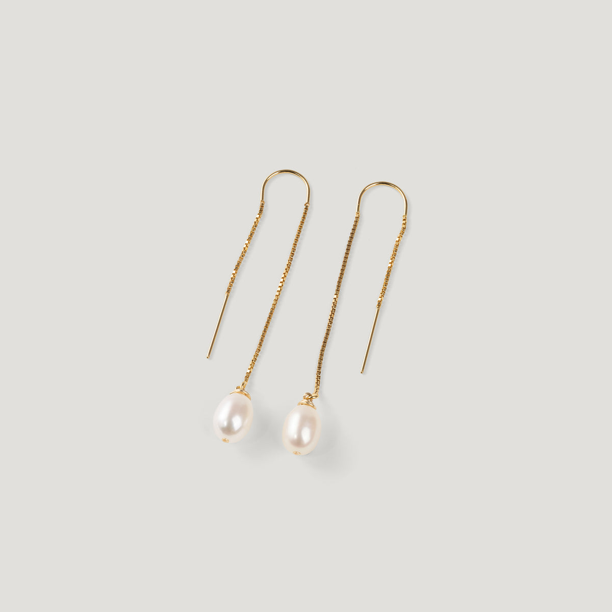 Pair of gold thread earrings, each with a dangling pearl, on light background.