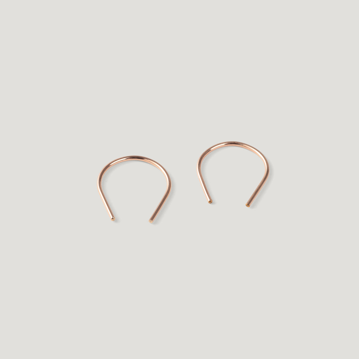 Pair of small rose gold thread earrings, a rounded arch shape on light background.