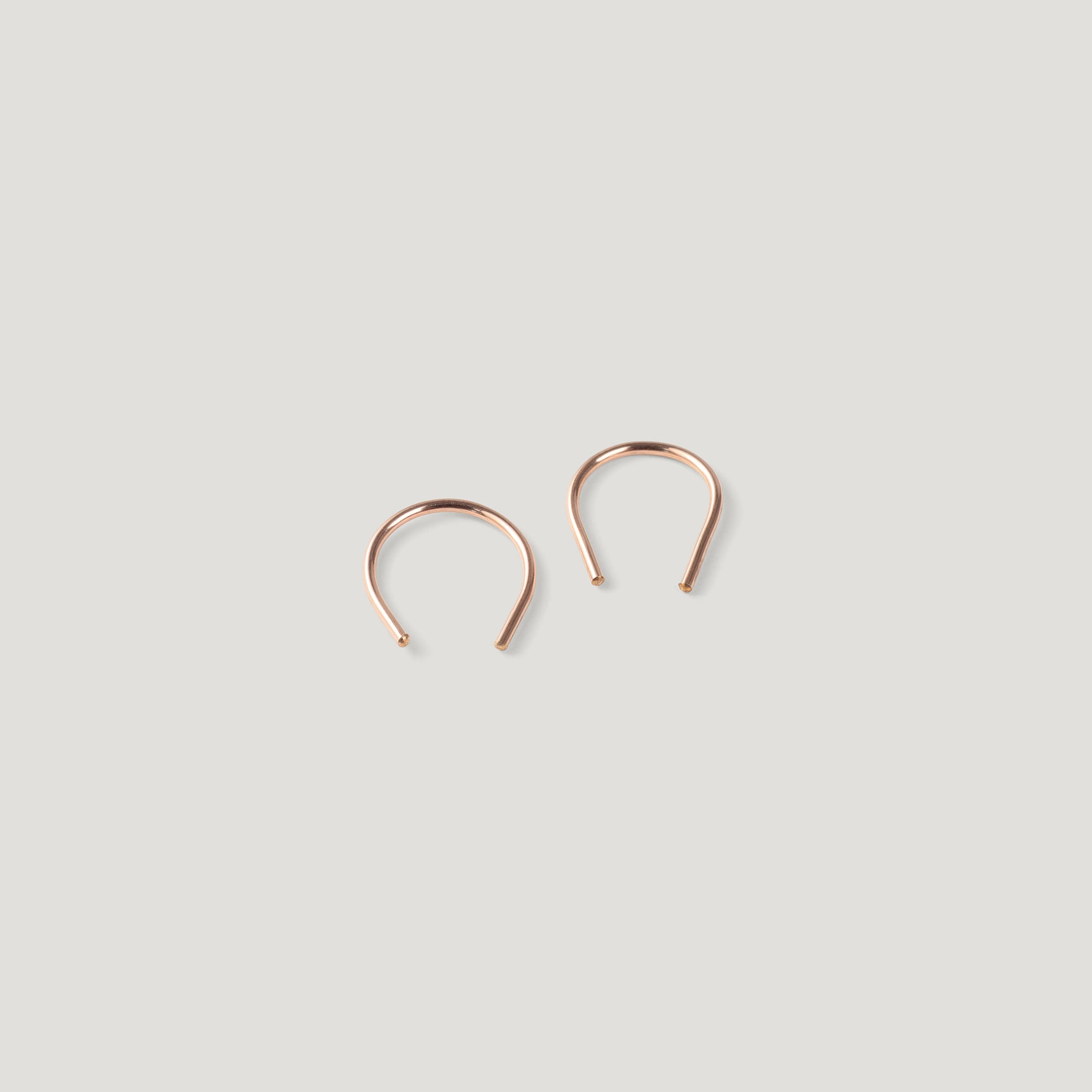 Pair of small rose gold thread earrings, one turned at an angle, close together.