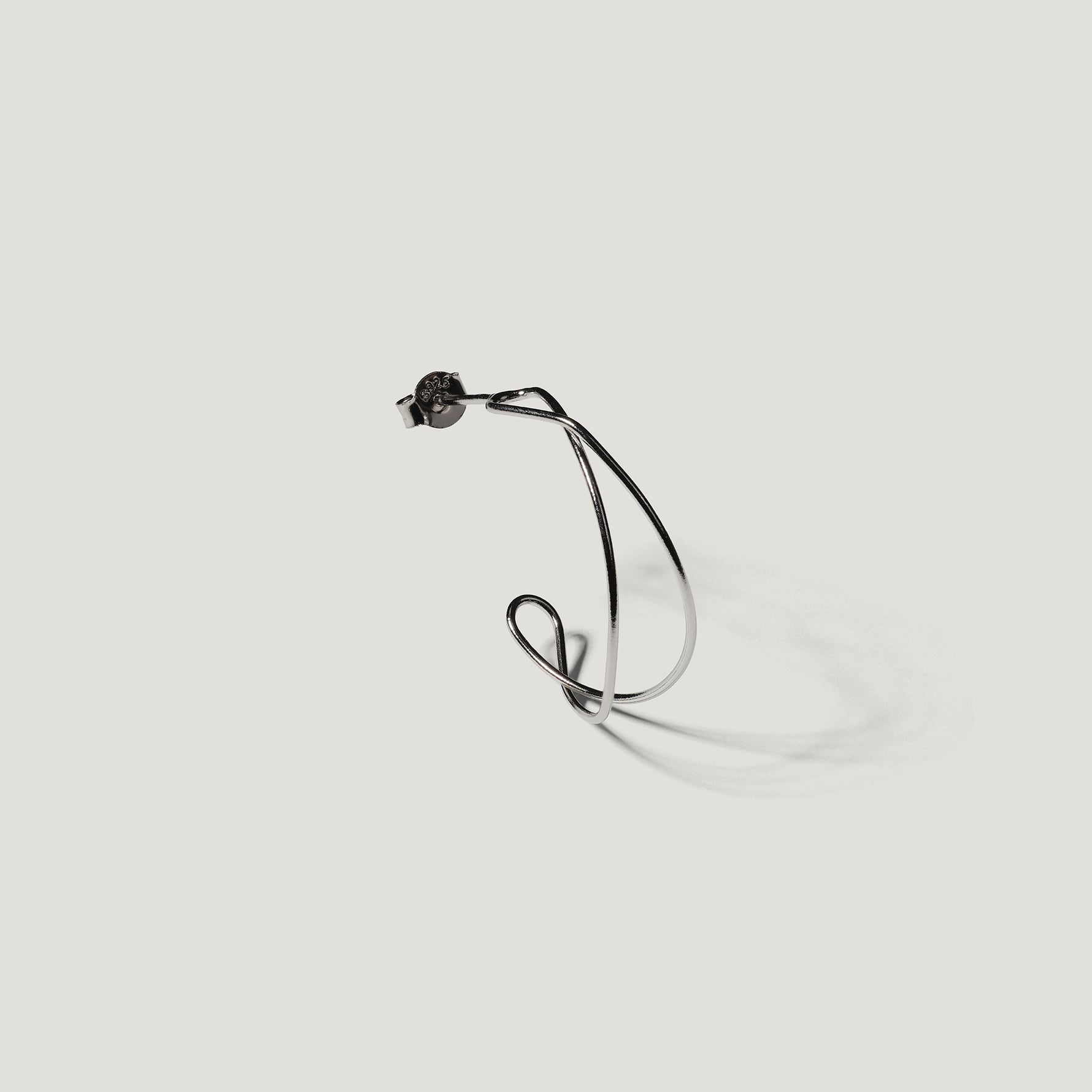 Single silver wire hoop earring shown from the side, close-up on light background.