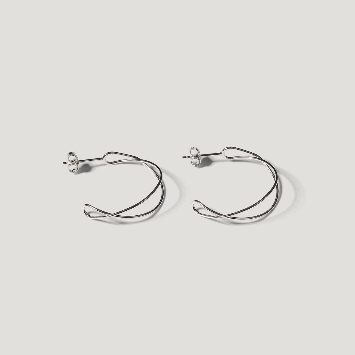 Pair of silver open wire hoop earrings with a twisted double-wire design, on light background.