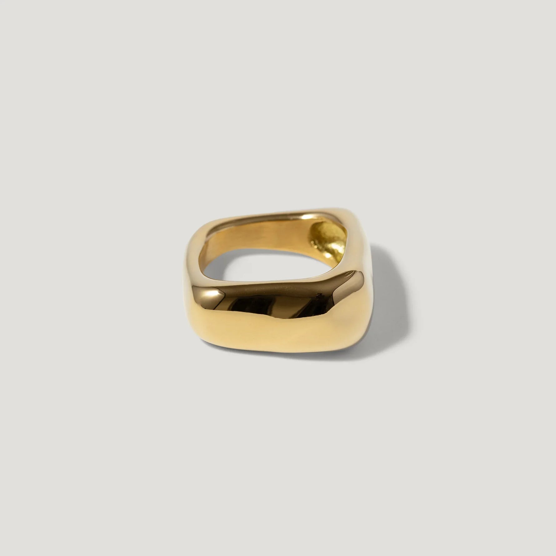 Modern square gold ring with polished finish on a neutral background