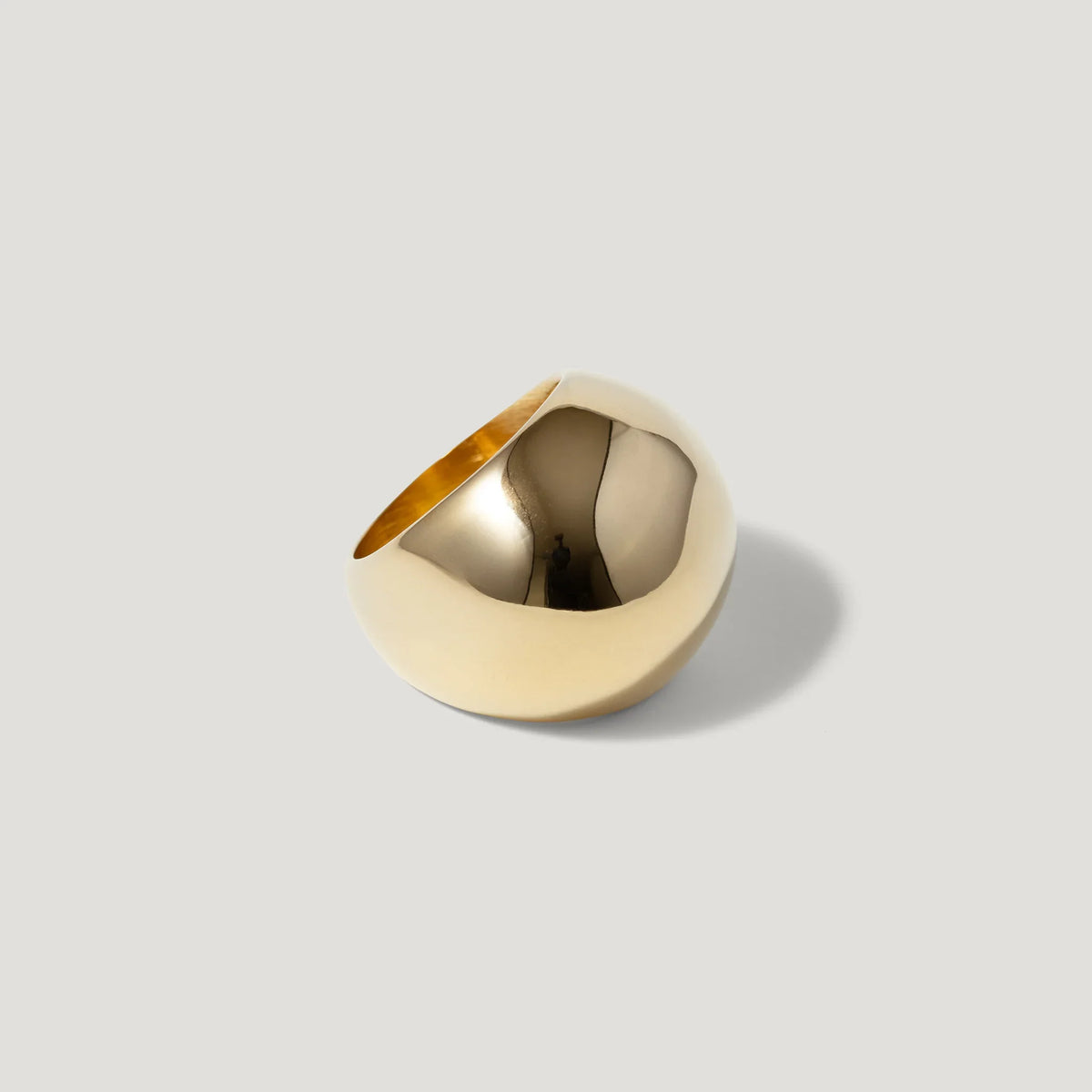Polished gold statement ring with a bold, modern, dome-shaped design on a neutral background