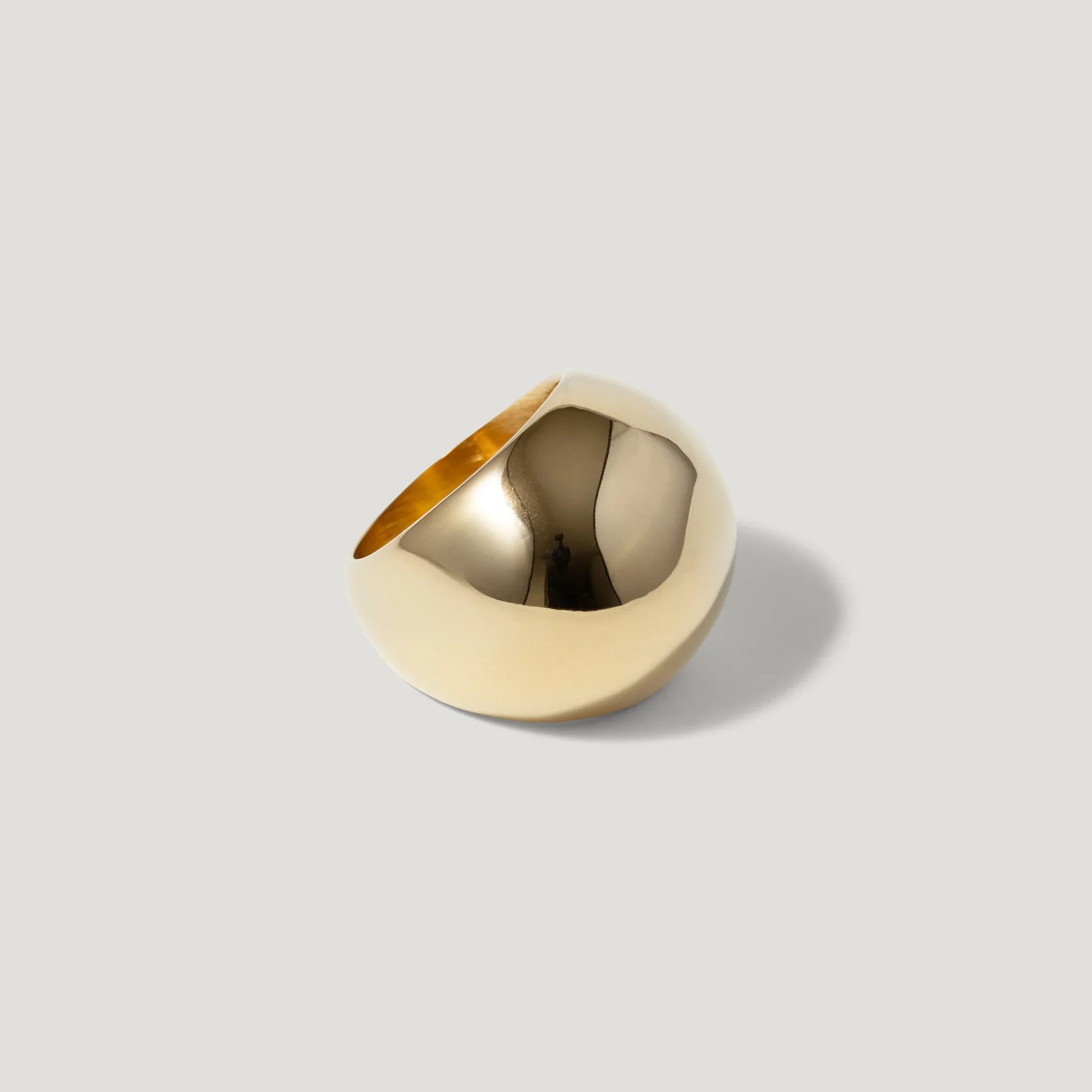 Polished gold statement ring with a bold, modern, dome-shaped design on a neutral background